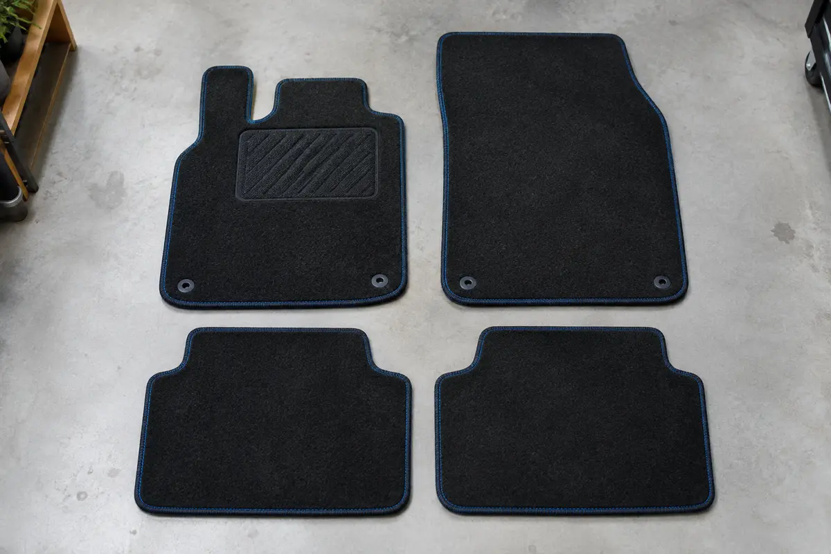 Quatre tapis universels en feutre noir à coutures bleues, dont un avec talonnette, posés à plat sur un sol de garage gris clair