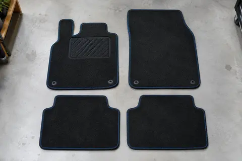 Quatre tapis universels en feutre noir à coutures bleues, dont un avec talonnette, posés à plat sur un sol de garage gris clair