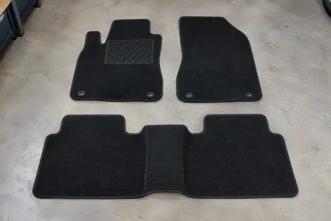Trois tapis sur mesure en moquette noire, deux avant et un tapis arrière d’une pièce, posés à plat sur un sol de garage gris clair