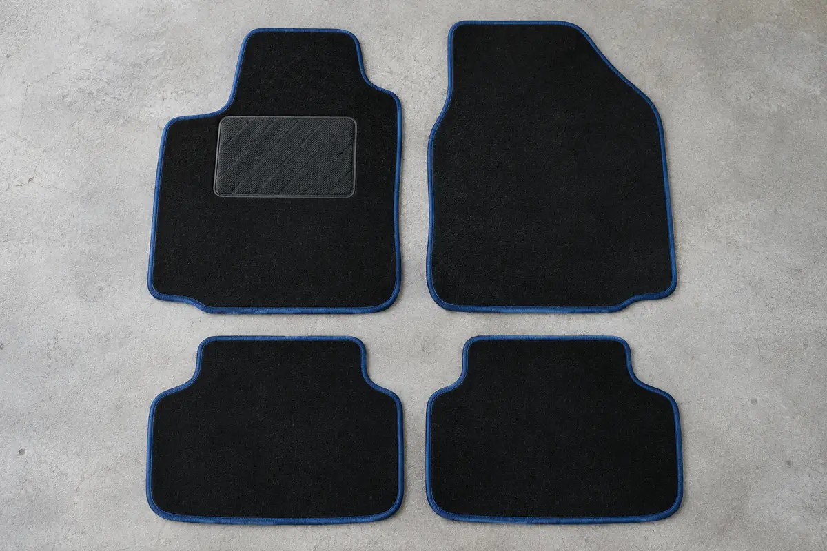 Quatre tapis universels en moquette noire à bordure bleue, dont un avec talonnette, posés à plat sur un sol de garage gris clair