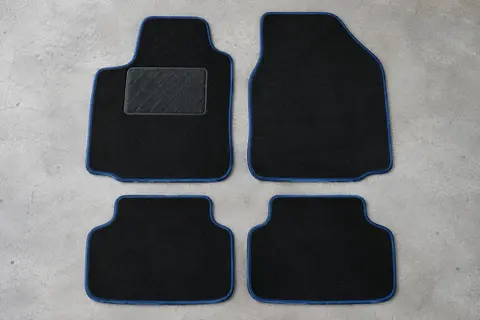 Quatre tapis universels en moquette noire à bordure bleue, dont un avec talonnette, posés à plat sur un sol de garage gris clair