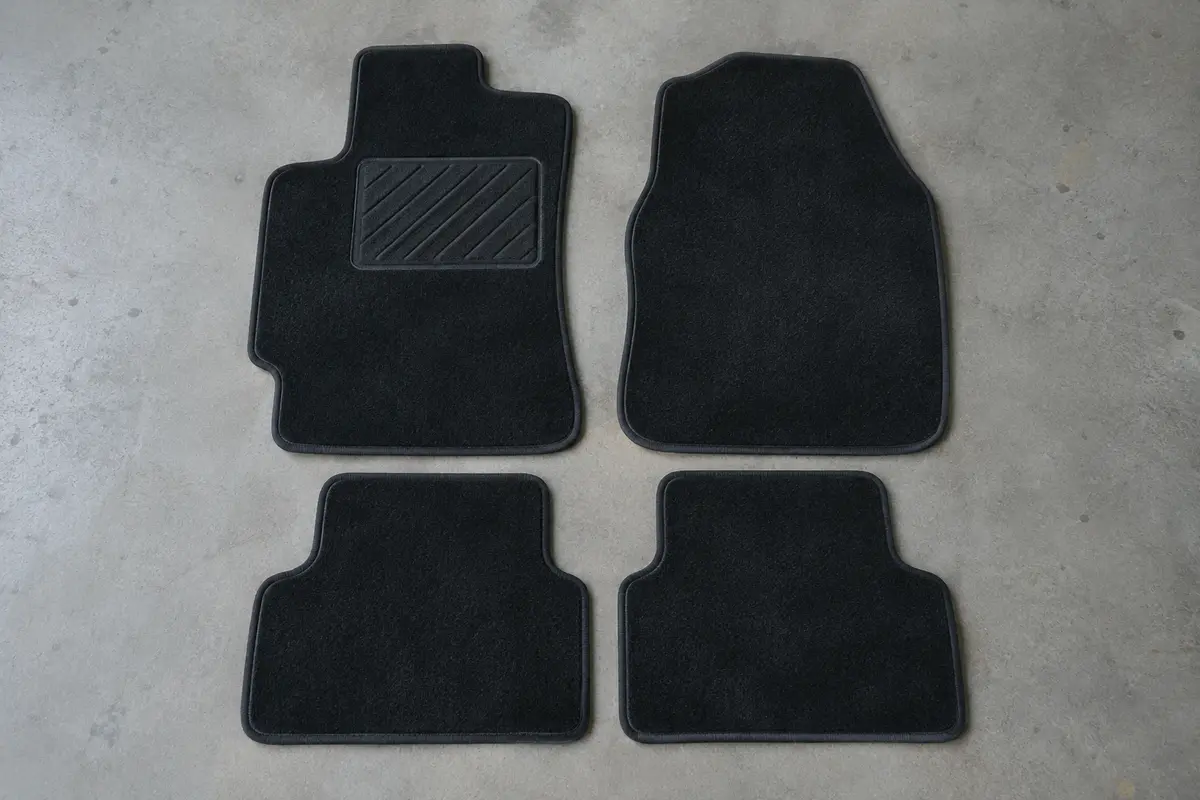 Quatre tapis de sol en velours noir bordés d’une ganse, posés à plat côte à côte, avec renfort au talon côté conducteur.