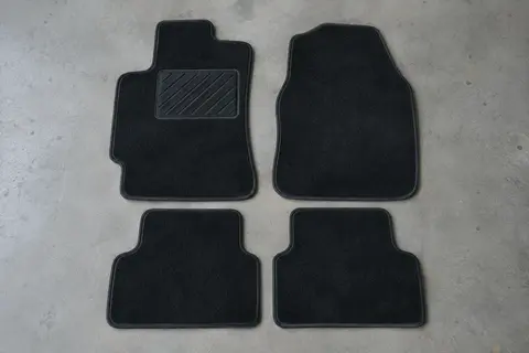 Quatre tapis de sol en velours noir bordés d’une ganse, posés à plat côte à côte, avec renfort au talon côté conducteur.