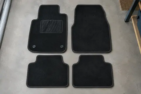 Quatre tapis de sol en velours noir posés à plat côte à côte, avec zone de talon renforcée côté conducteur.