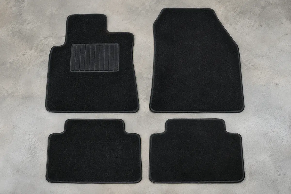 Quatre tapis sur mesure en velours noir à bordure renforcée, posés à plat sur un sol de garage gris clair
