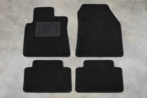 Quatre tapis sur mesure en velours noir à bordure renforcée, posés à plat sur un sol de garage gris clair