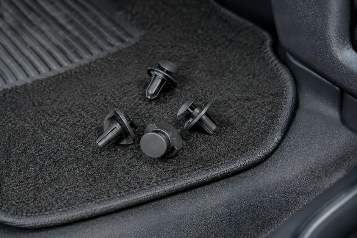 Quatre clips noirs en nylon avec boucles circulaires, posés près d’un tapis de sol automobile