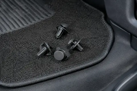 Quatre clips noirs en nylon avec boucles circulaires, posés près d’un tapis de sol automobile
