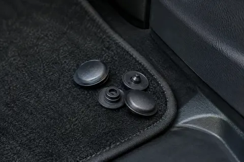 Fixations noires à bouton-pression posées près d’un tapis de sol dans un habitacle automobile propre