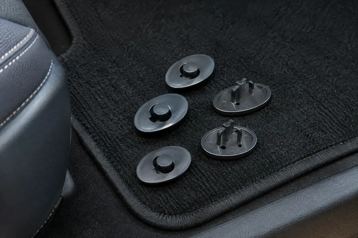 Fixations ovales métalliques anthracite à clips tournants près d’un tapis de voiture noir.