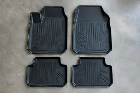 Quatre tapis moulés en TPE noir à bords hauts, posés à plat sur un sol de garage gris clair
