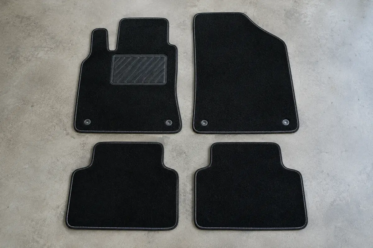 Quatre tapis sur mesure en moquette noire à surpiqûre blanche, dont un avec talonnette, posés à plat sur un sol de garage gris clair