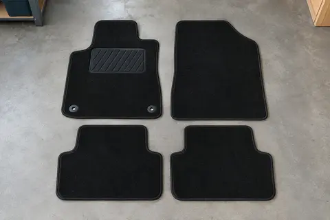 Quatre tapis sur mesure en moquette noire, dont un avec talonnette en caoutchouc, posés à plat sur un sol de garage gris clair