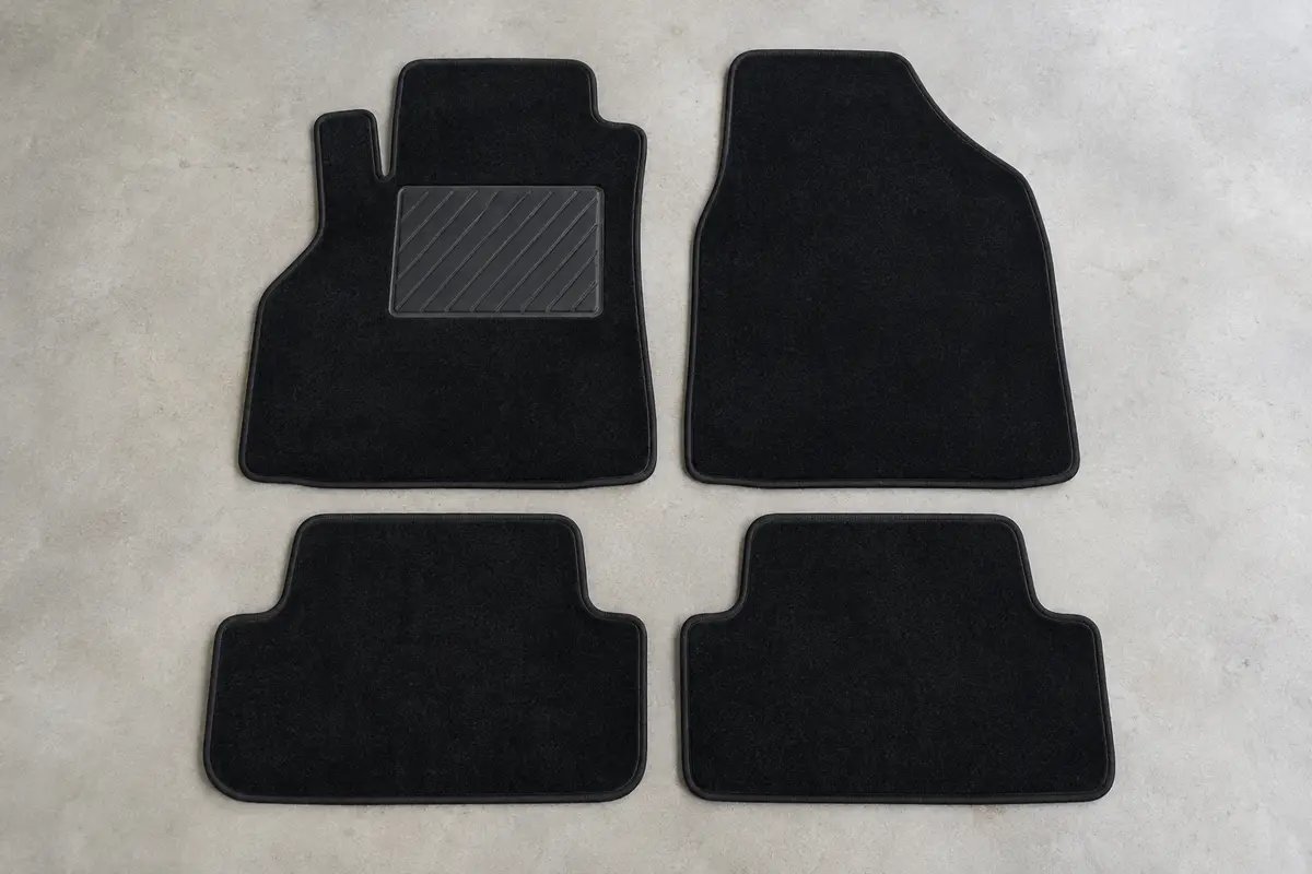 Quatre tapis sur mesure en velours noir, dont un avec talonnette en caoutchouc, posés à plat sur un sol de garage gris clair