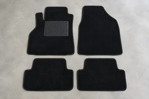 Quatre tapis sur mesure en velours noir, dont un avec talonnette en caoutchouc, posés à plat sur un sol de garage gris clair