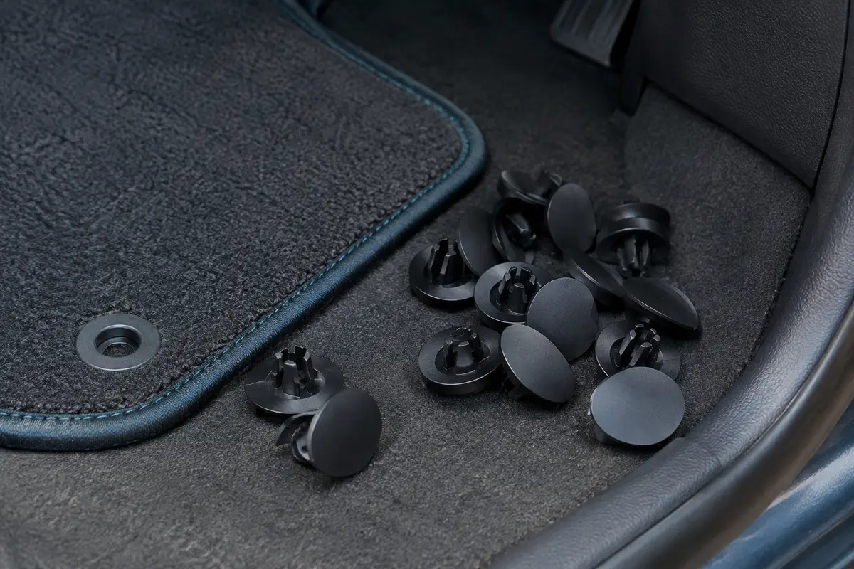 Clips ronds noirs de fixation pour tapis auto, disposés près d’un tapis de sol dans un habitacle propre.