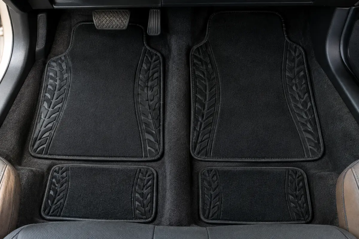 Quatre tapis de sol noirs en polyester, avec motif de pneus en relief sur les côtés, posés dans un habitacle automobile.