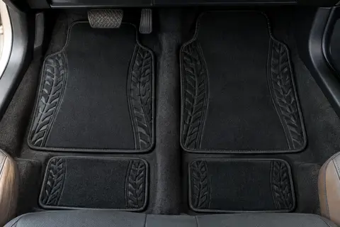 Quatre tapis de sol noirs en polyester, avec motif de pneus en relief sur les côtés, posés dans un habitacle automobile.