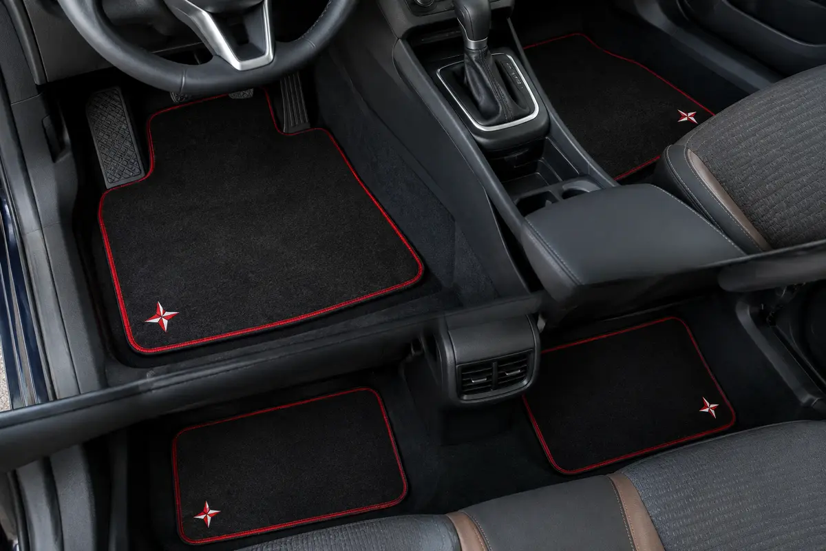 Jeu de quatre tapis auto en moquette noire à bordure rouge, ornés d’une petite étoile brodée rouge et blanche, dans un habitacle propre.
