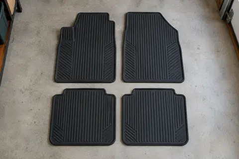 Quatre tapis universels en caoutchouc noir rainuré, deux grands et deux petits, posés à plat sur un sol de garage gris clair
