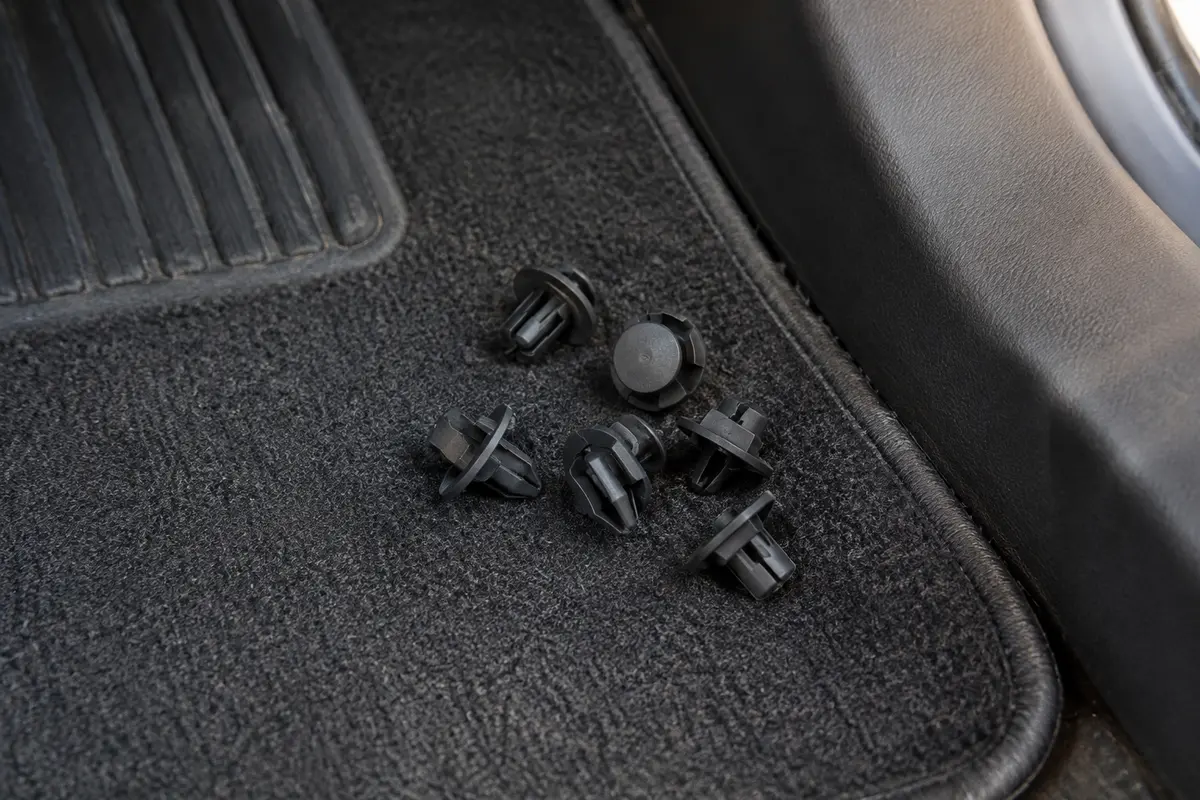 Clips de fixation noirs en nylon posés près du bord d’un tapis de sol automobile