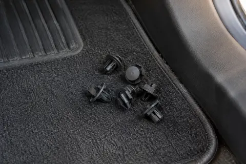 Clips de fixation noirs en nylon posés près du bord d’un tapis de sol automobile
